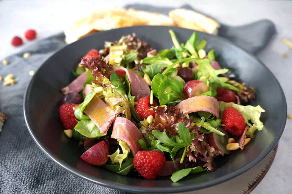 grüner Salat mit gemischten Salatblättern, Roastbeef, Himbeeren, Weintrauben und Honig-Senf Dressing, Pinienkernen und gerösteten Fladenbrot
